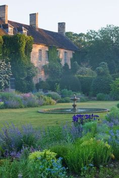 the garden is full of colorful flowers and plants in front of an old house with stone chimneys