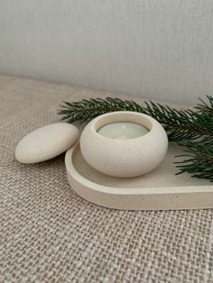 a white candle sitting on top of a wooden stand next to a pine tree branch