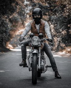 a man riding on the back of a motorcycle down a road with trees in the background