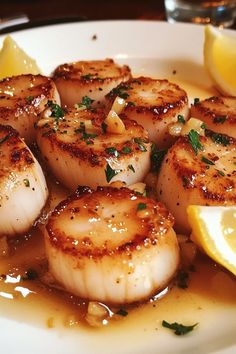 some scallops are sitting on a plate with lemon wedges