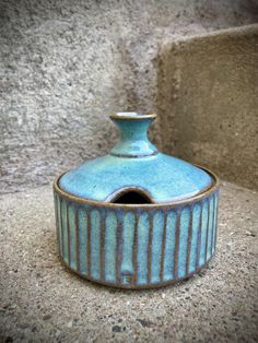 a small blue vase sitting on top of a cement floor next to a stone wall