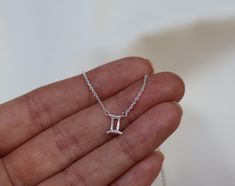 a hand holding a tiny silver necklace with the letter i on it's side