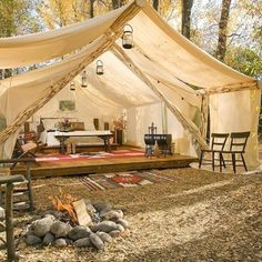 a tent is set up in the woods with chairs around it and a fire pit