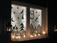 candles are lit in front of a window decorated with paper houses and trees, which look like they have been drawn on