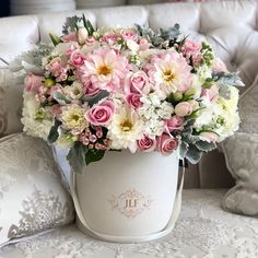 a bouquet of pink and white flowers sitting in a bucket on a couch next to pillows