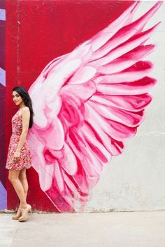 a woman standing in front of a wall with pink wings painted on it