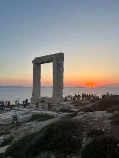 the sun is setting behind an ancient greek temple near the ocean with people standing around it