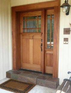 a wooden front door with two sidelights and a bench on the porch next to it