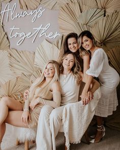 four women posing for a photo in front of a wall with palm leaves