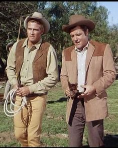 two men in cowboy hats are standing next to each other with one holding a rope