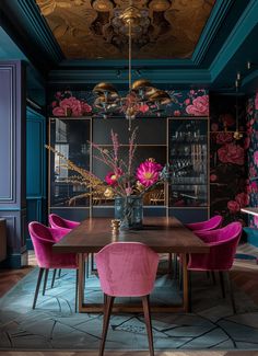 a dining room with blue walls, pink chairs and a wooden table in the center