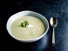 a white bowl filled with broccoli soup next to a silver spoon on a black surface