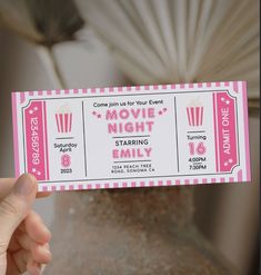 a person holding up a pink and white ticket for a movie night with popcorn on it