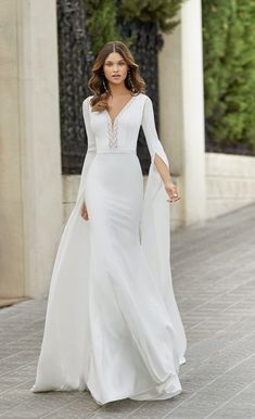 a woman in a white wedding dress walking down the street with her arms outstretched and wearing a cape