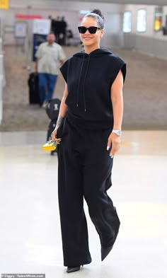 a woman in black is walking through an airport with her hand on her hip and wearing sunglasses