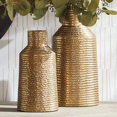 two gold vases sitting next to each other with green leaves on top of them