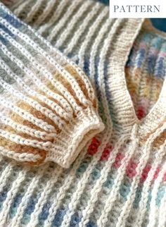 a knitted sweater sitting on top of a bed next to a blue and white blanket