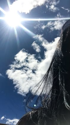 the back of a woman's head with clouds in the background and sun shining through her hair