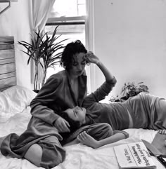 a woman sitting on top of a bed next to a book and plant in front of her