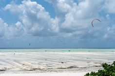 people parasailing in the ocean on an overcast day with blue skies and white sand