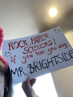 a woman holding up a sign that says rock paper scissors? if you lose you sing mr brightside