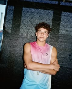 a young man standing in front of a wall with his arms crossed and looking at the camera