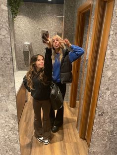 two women standing in front of a mirror taking a selfie with their cell phone