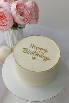 a birthday cake with the words happy birthday on it and pink flowers in a vase