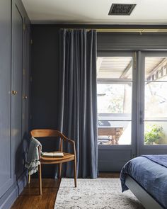 a bedroom with dark blue walls and wooden flooring, along with a large window