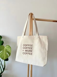 a canvas tote bag with coffee and more coffee printed on it hanging from a coat rack