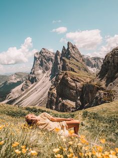 a woman laying in the grass with mountains in the background