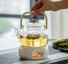 a person holding a tea pot over a kettle filled with green tea on top of a table