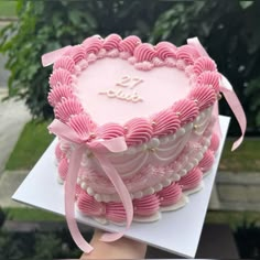 a heart shaped cake with pink icing and bows on it's edges is being held by a person