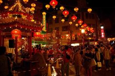 many people are walking around in the street with lanterns hanging from the ceiling above them