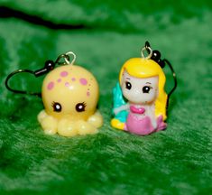 two little toys are sitting next to each other on a green surface, one has a yellow octopus in it's mouth and the other is wearing a pink dress