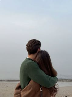 a man and woman are hugging on the beach with a kite in the sky above them