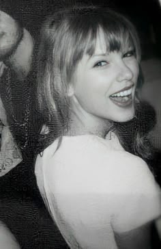 a black and white photo of a woman with blue eyes smiling at the camera while another man looks on