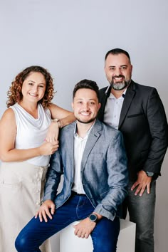 three people standing next to each other in front of a white wall and one person is smiling at the camera