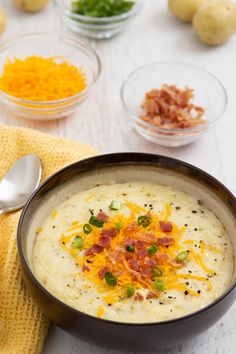 a bowl of potato soup with bacon, cheese and green onions next to bowls of other ingredients