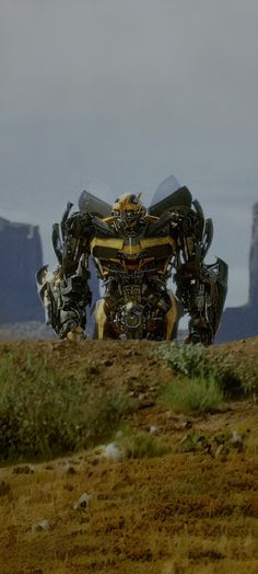 a large robot standing on top of a grass covered field in front of some mountains