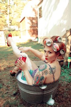 a tattooed woman sitting in a tub with cans on her head and holding a can