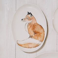 a plate with a painting of a fox sitting on top of it next to two plates