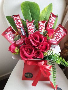 a vase filled with roses and chocolates on top of a white chair next to a plant