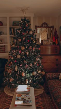 a living room with a christmas tree in the corner and books on the coffee table