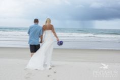 a bride and groom walking on the beach holding hands with an ocean in the background