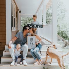 a family sitting on the porch with a sold sign