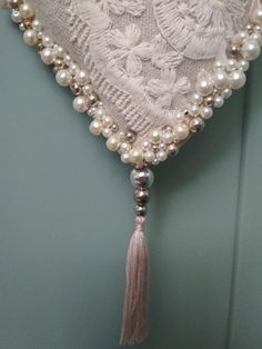 a white heart with pearls and tassels hanging from it's side on a wall