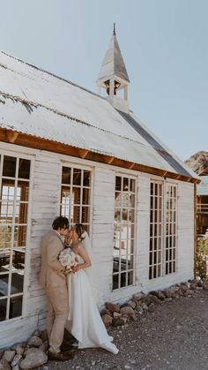 a bride and groom kissing in front of an old white building with large open windows