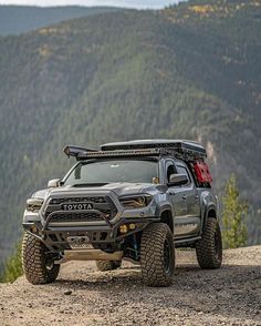 a gray toyota truck parked on top of a mountain with mountains in the back ground