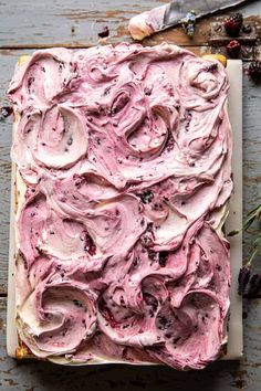 a square cake with pink frosting and berries on top, next to a knife